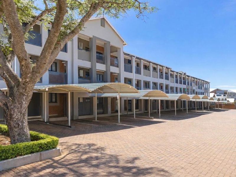 Front elevation of the townhouse complex featuring a paved driveway, covered parking bays, and multi-level residential units with balconies.