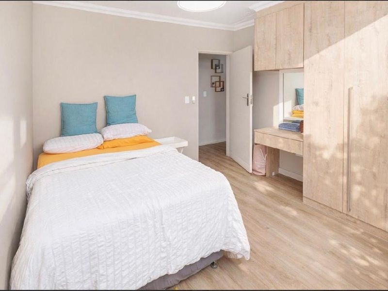 A well-maintained bedroom featuring light wood-look laminate flooring, built-in cabinetry with an integrated vanity, and neutral wall finishes.