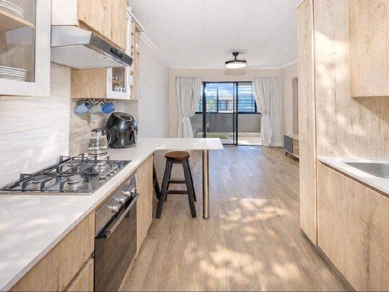 Modern open-plan kitchen and living area featuring light wood cabinetry, gas hob, and seamless flow to a private balcony through sliding glass doors.