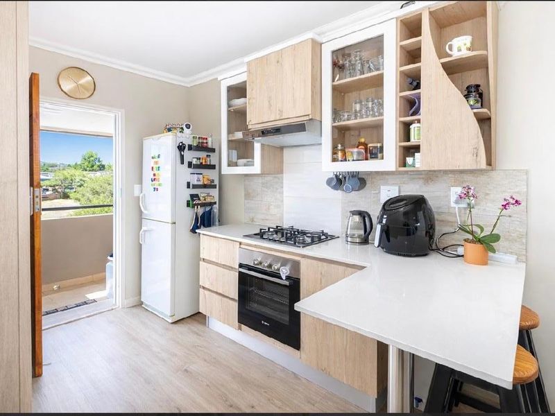 Modern kitchen featuring light wood cabinetry, stone countertops, gas hob, built-in oven, and direct access to an outdoor balcony area.
