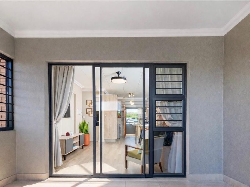 A covered patio area featuring tiled flooring, coved ceilings, and a large sliding glass door with security bars providing access to the interior living space.