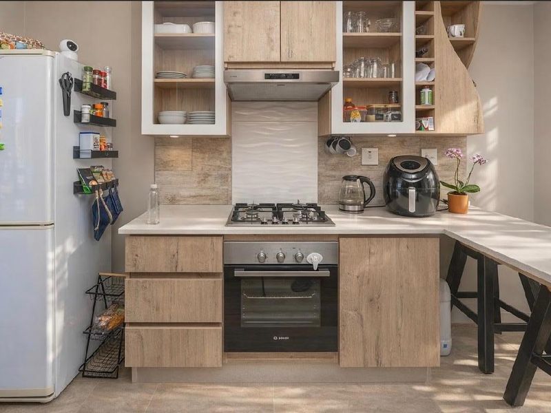 A modern, well-maintained kitchen featuring light wood-finish cabinetry, a gas hob, built-in oven, extractor fan, and stone countertops with a breakfast nook.