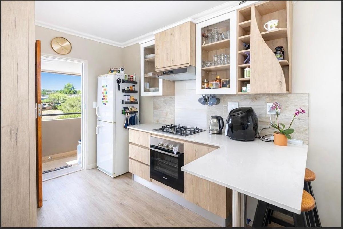 Modern kitchen featuring light wood cabinetry, stone countertops, gas hob, built-in oven, and direct access to an outdoor balcony area.