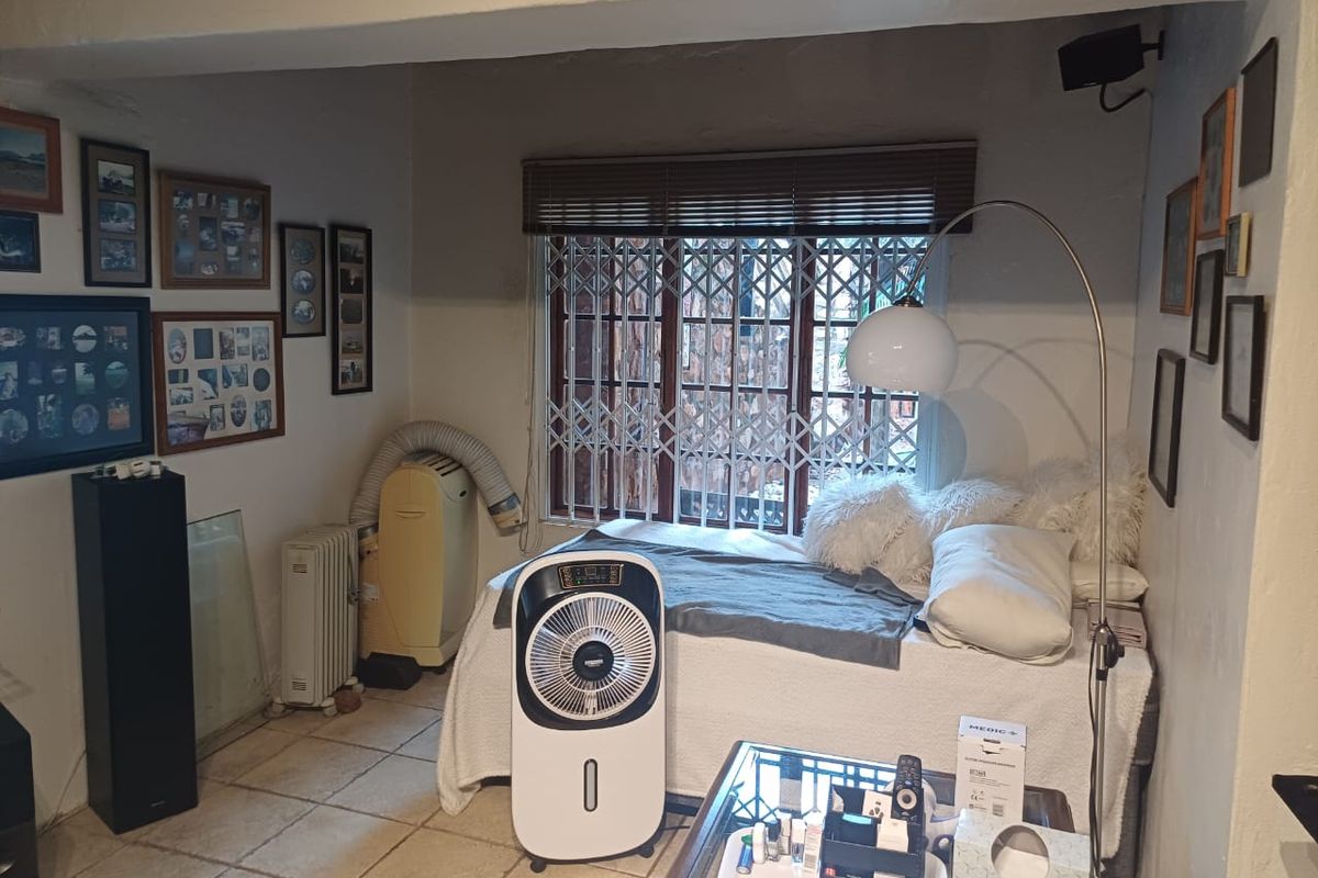 A bedroom featuring tiled flooring, a window with security gate, and blinds, providing a functional space for rest.