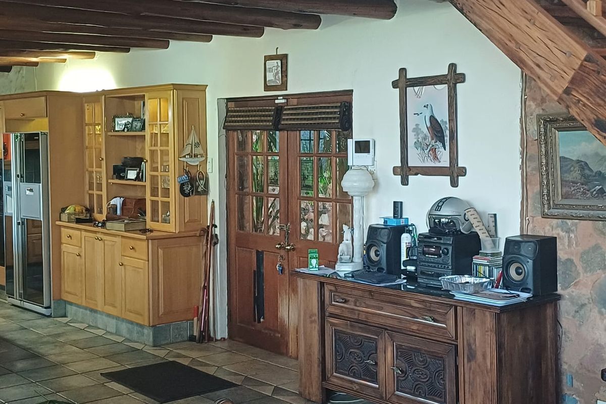 A rustic living area featuring exposed timber ceiling beams, a stone feature wall, tiled flooring, and built-in wooden cabinetry with timber-framed double doors.