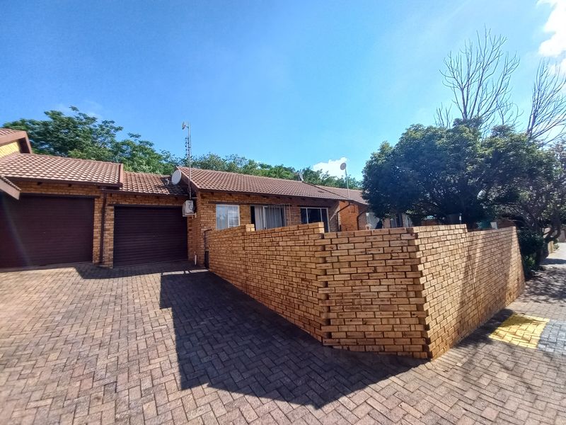 Front exterior view of a townhouse featuring a brick facade, tiled roof, paved driveway, and a private brick boundary wall.