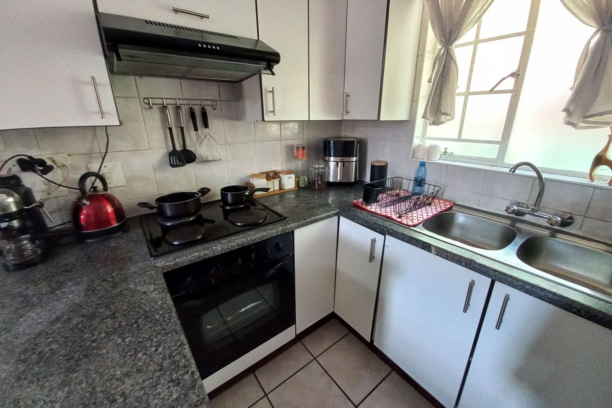 A functional kitchen featuring white cabinetry, dark laminate countertops, a built-in oven with hob, extractor fan, and a double bowl stainless steel sink.