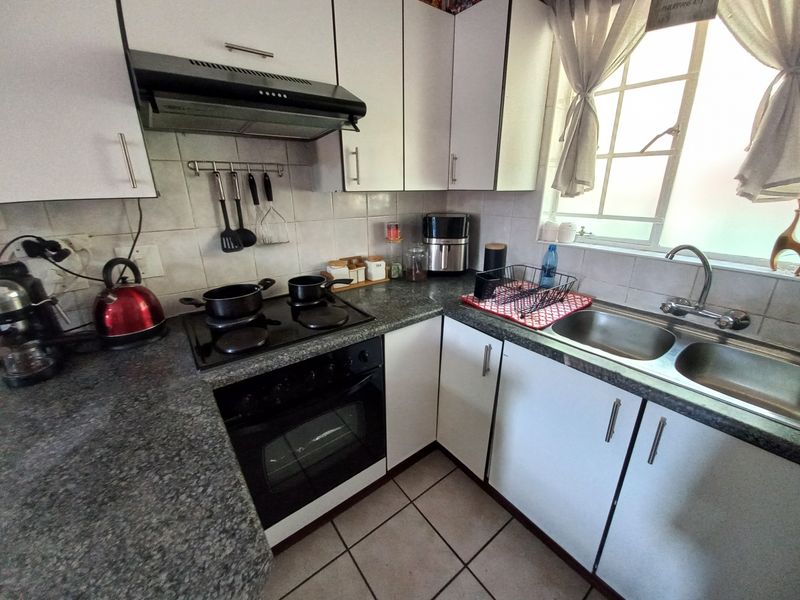 A functional kitchen featuring white cabinetry, dark laminate countertops, a built-in oven with hob, extractor fan, and a double bowl stainless steel sink.