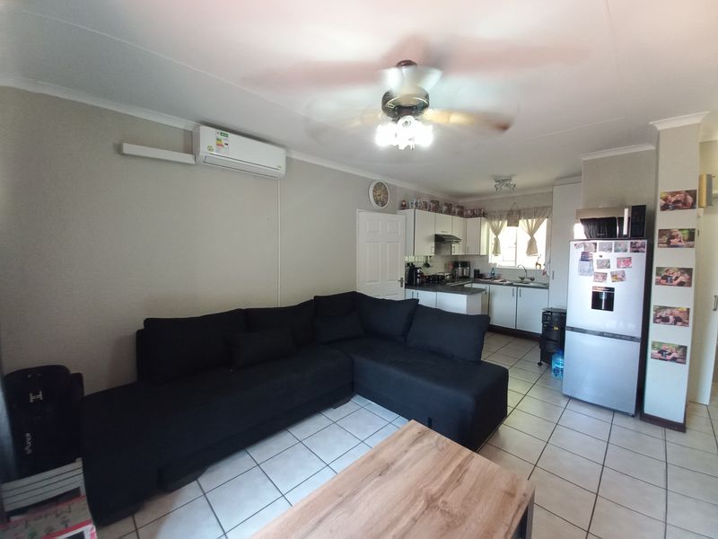 Open-plan living area featuring tiled floors, a ceiling fan, and an air conditioning unit, seamlessly connected to a functional kitchen space.