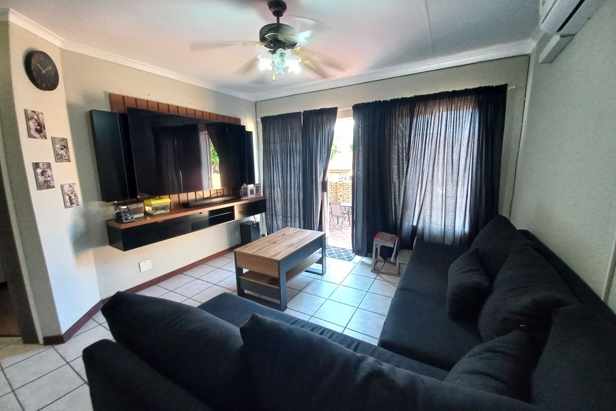 A comfortable living room featuring tiled flooring, a ceiling fan, wall-mounted air conditioning, and a sliding glass door providing access to the patio.