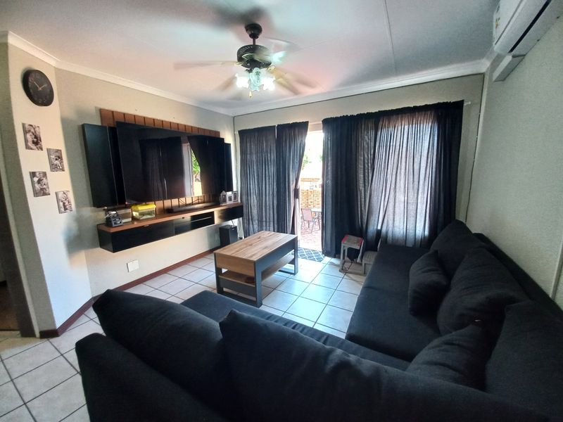 A comfortable living room featuring tiled flooring, a ceiling fan, wall-mounted air conditioning, and a sliding glass door providing access to the patio.