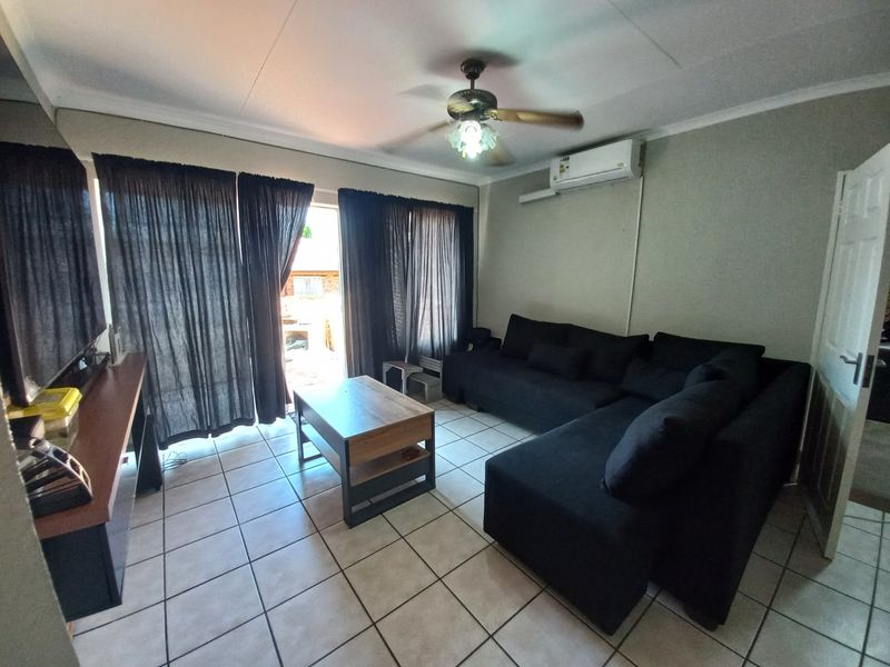 A functional living room featuring tiled flooring, a ceiling fan, and a wall-mounted split-system air conditioner, with direct access to an outdoor area.