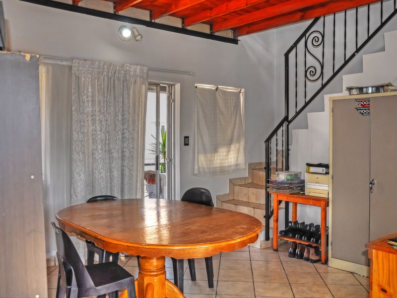 Open plan living area featuring exposed timber ceiling beams, tiled flooring, and a wrought iron staircase leading to the upper level.