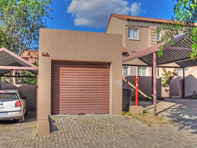 Exterior view of a single garage unit with a roller shutter door, adjacent carport, and paved driveway area.
