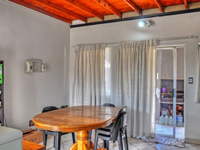 Dining area featuring exposed timber ceiling beams, tiled flooring, and direct access to an outdoor patio with a built-in braai.