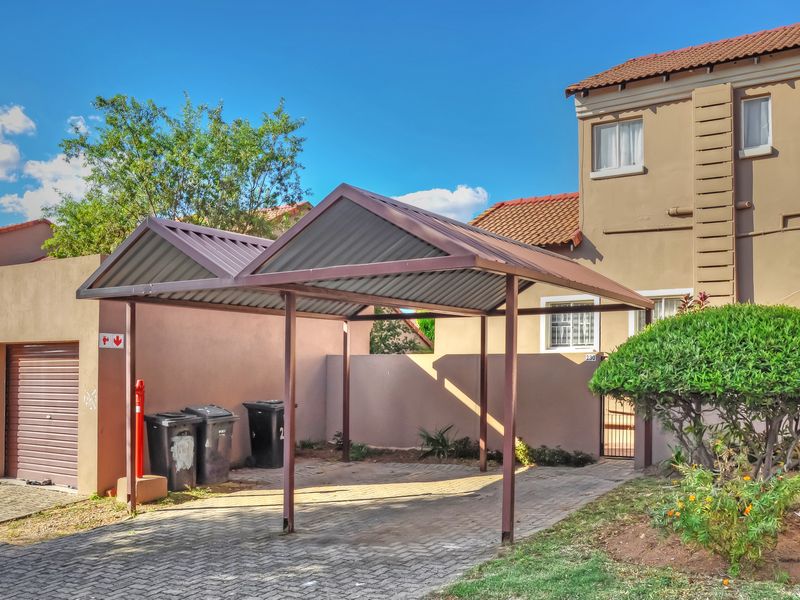 Front exterior view of the apartment featuring a double metal carport, paved driveway, and a secure roller shutter garage door.