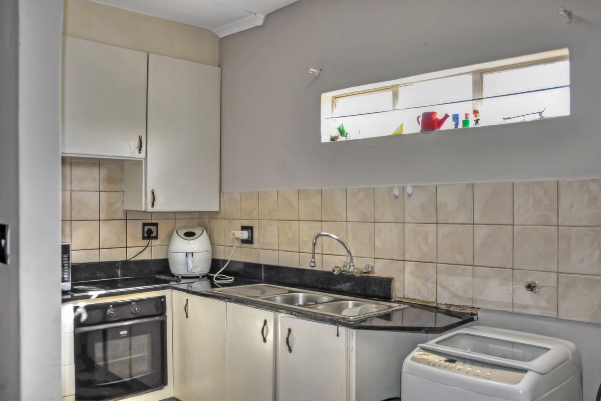 A functional kitchen featuring built-in cabinetry, granite countertops, a stainless steel sink, and integrated oven and hob with tiled backsplash.