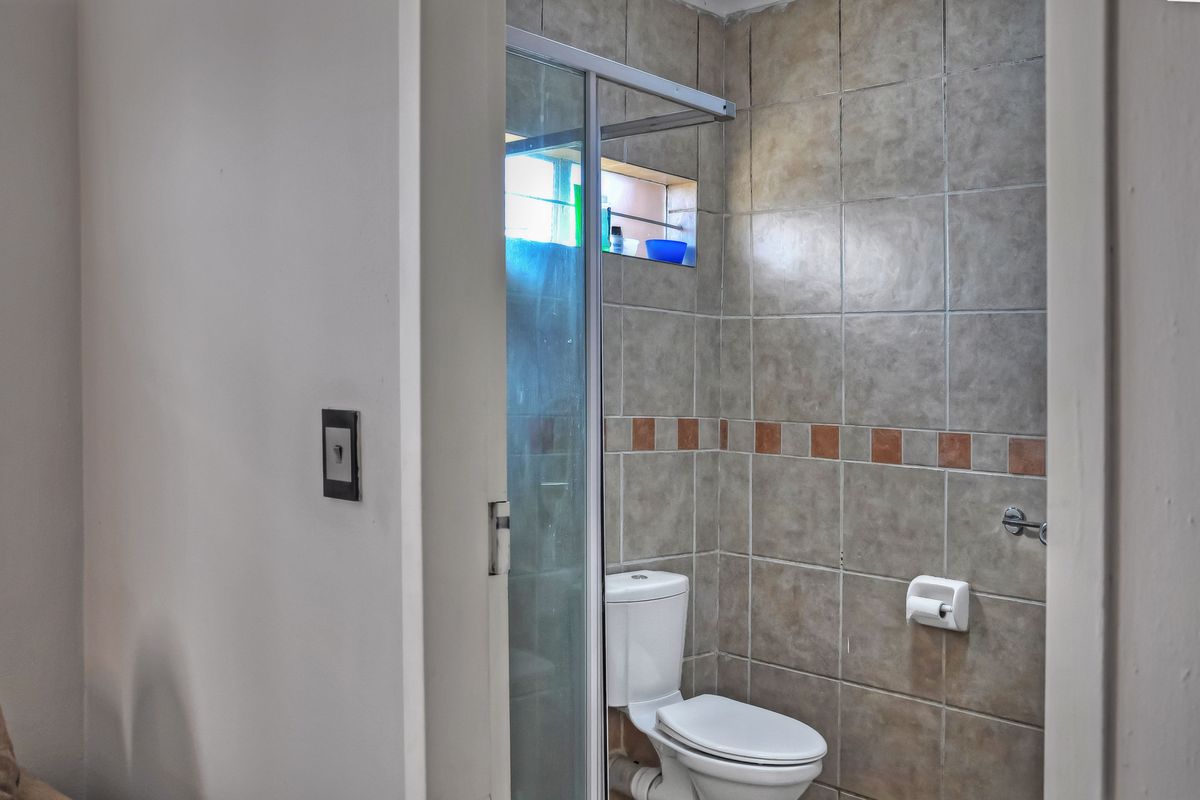 A compact bathroom featuring a shower enclosure and toilet with dated wall tiling.