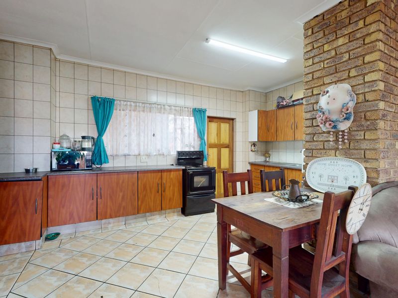 Open-plan kitchen and dining area featuring tiled flooring, an exposed brick feature pillar, and dated wooden cabinetry with a tiled splashback.