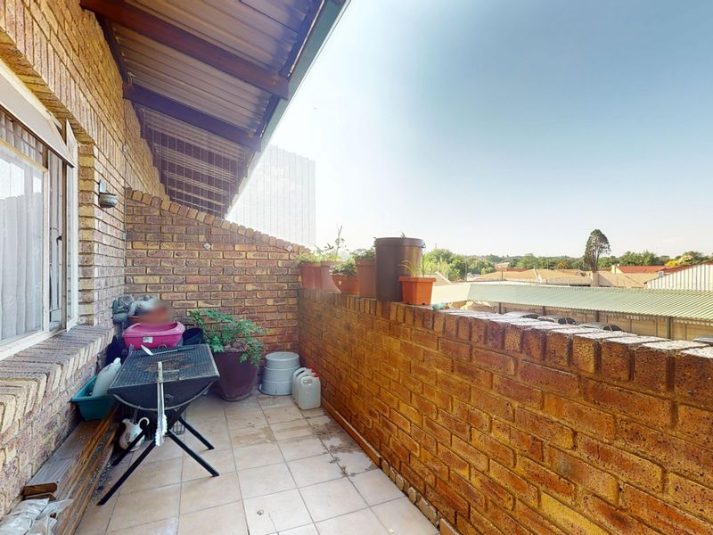 A covered balcony featuring face brick walls and tiled flooring, offering an outdoor space with views of the surrounding neighborhood.