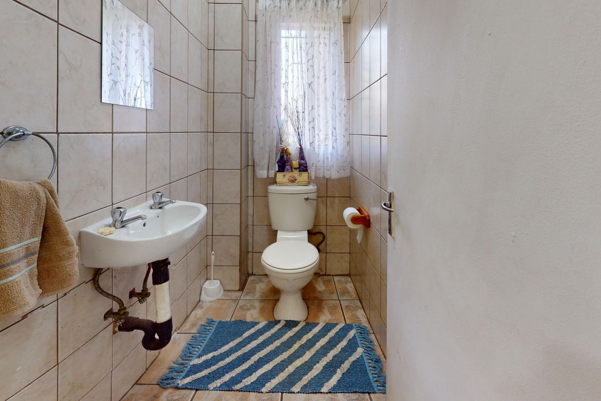 A compact guest bathroom featuring a wall-mounted basin and toilet with neutral ceramic wall and floor tiling.