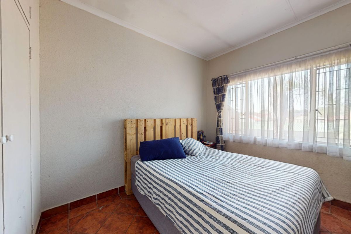 A bedroom featuring terracotta floor tiles, a built-in wardrobe, and a window fitted with security bars.