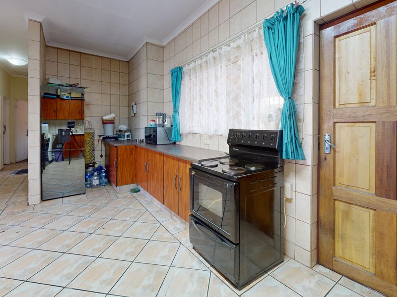 A functional kitchen featuring tiled flooring, wall-to-wall tiling, laminate cabinetry, and a freestanding stove with direct access to an adjacent hallway.