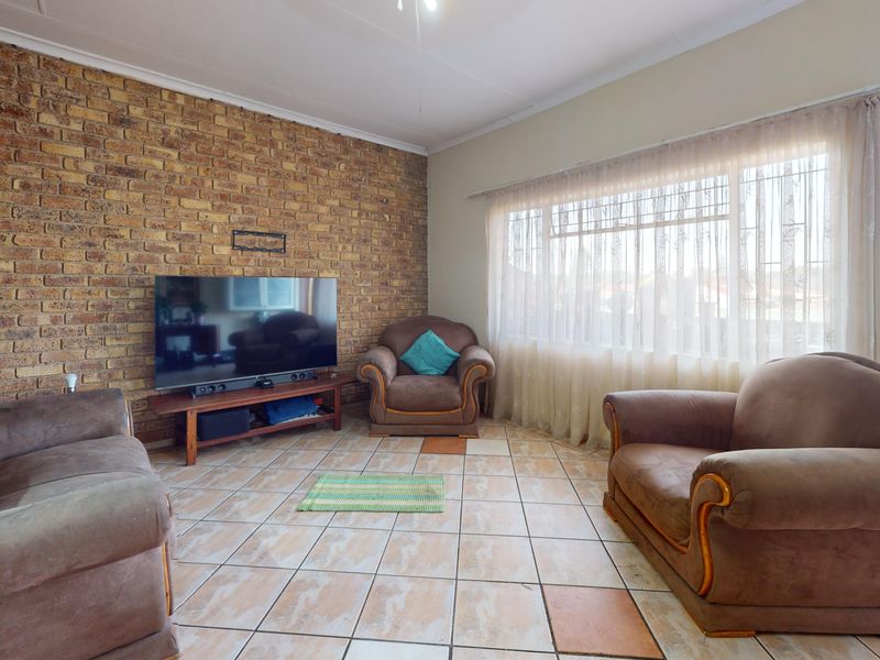 A living room featuring an exposed brick wall, ceramic tiled flooring, and a large window allowing natural light into the space.