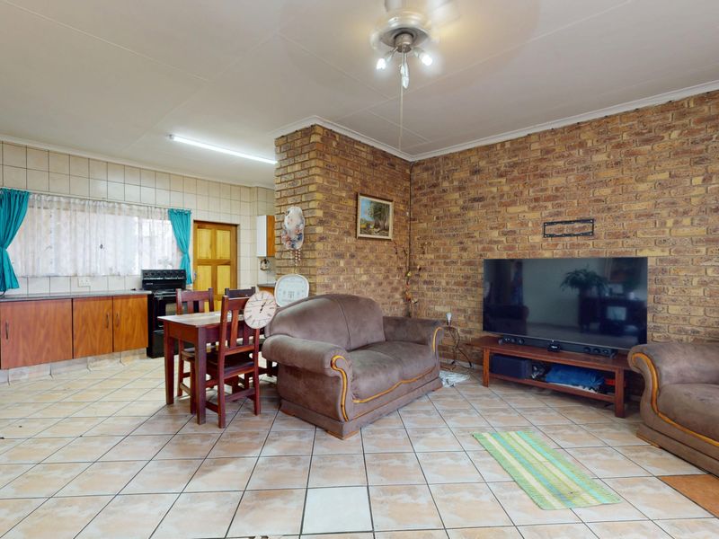 Open-plan living and kitchen area featuring exposed brick walls, tiled flooring, and functional kitchen cabinetry with a freestanding stove.