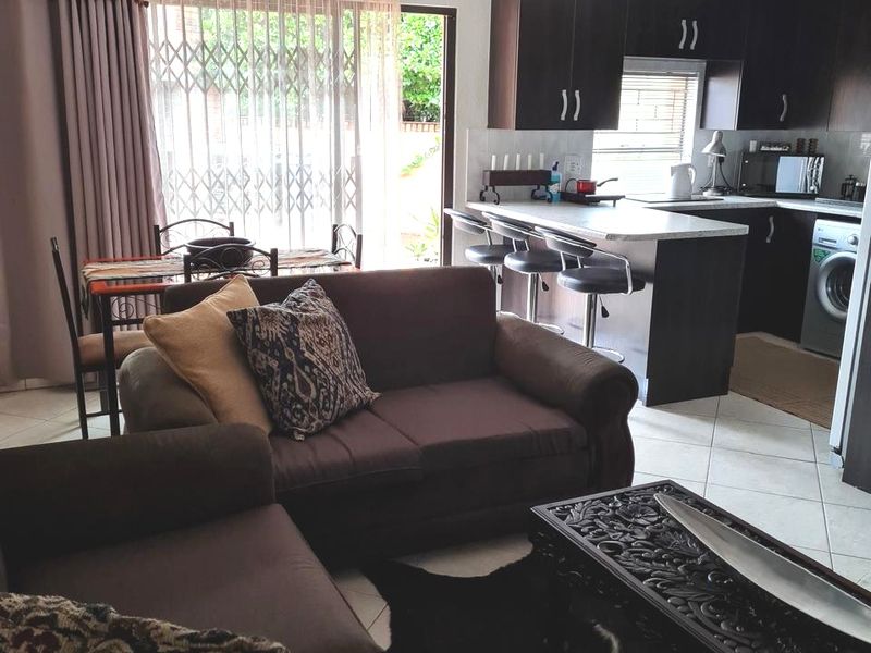Open-plan living and kitchen area featuring tiled floors, a breakfast bar, and direct access to the exterior through a sliding door with security gate.