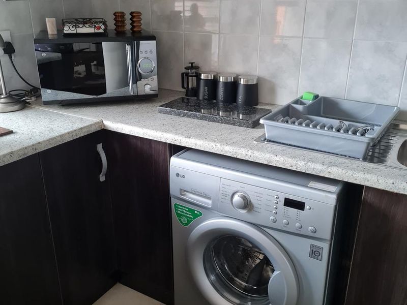 A functional kitchen area featuring dark wood-look cabinetry, light speckled countertops, ceramic wall tiling, and an integrated washing machine space.
