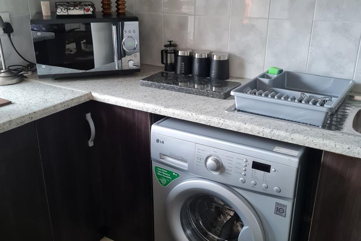 A functional kitchen area featuring dark wood-look cabinetry, light speckled countertops, ceramic wall tiling, and an integrated washing machine space.