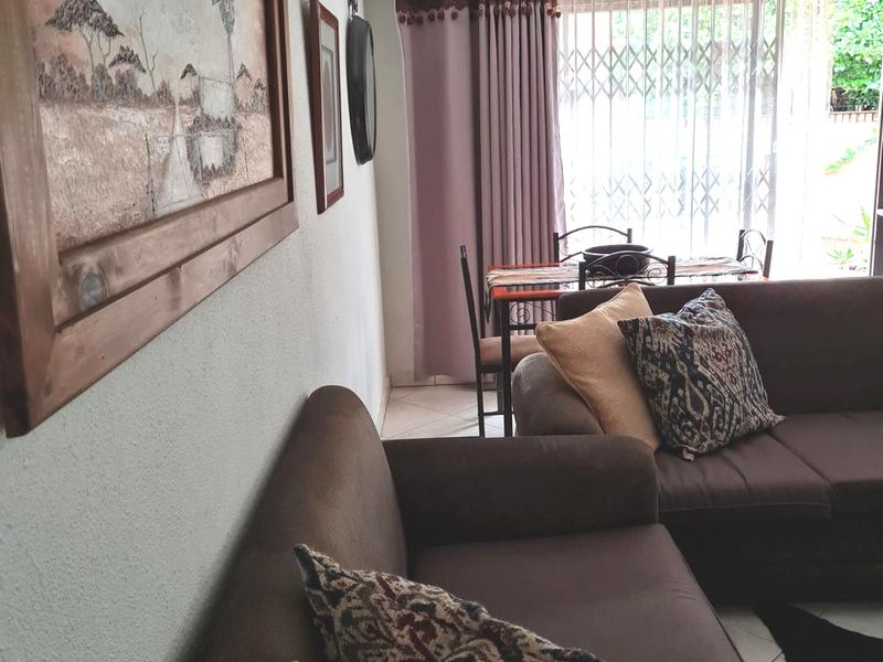 A comfortable living room area featuring tiled flooring, a ceiling fan, and a sliding glass door with security gate leading to the exterior.
