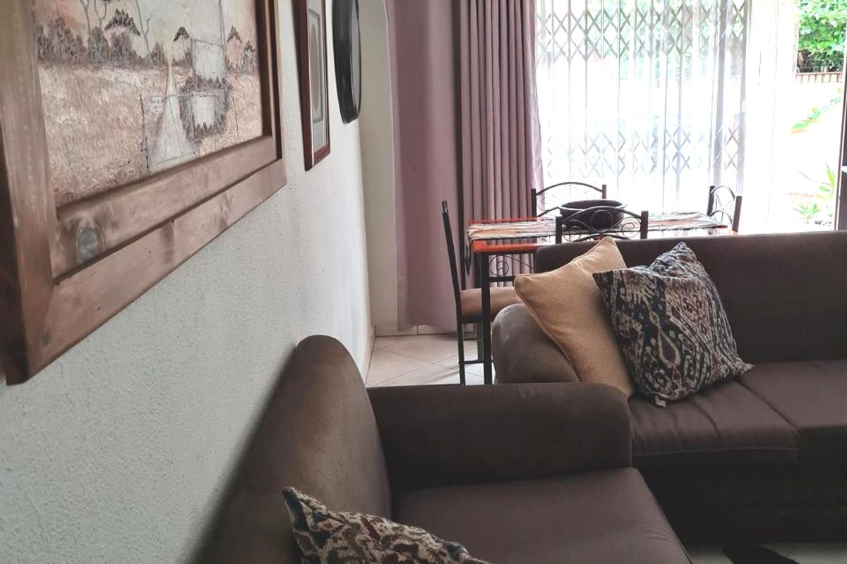 A comfortable living room area featuring tiled flooring, a ceiling fan, and a sliding glass door with security gate leading to the exterior.