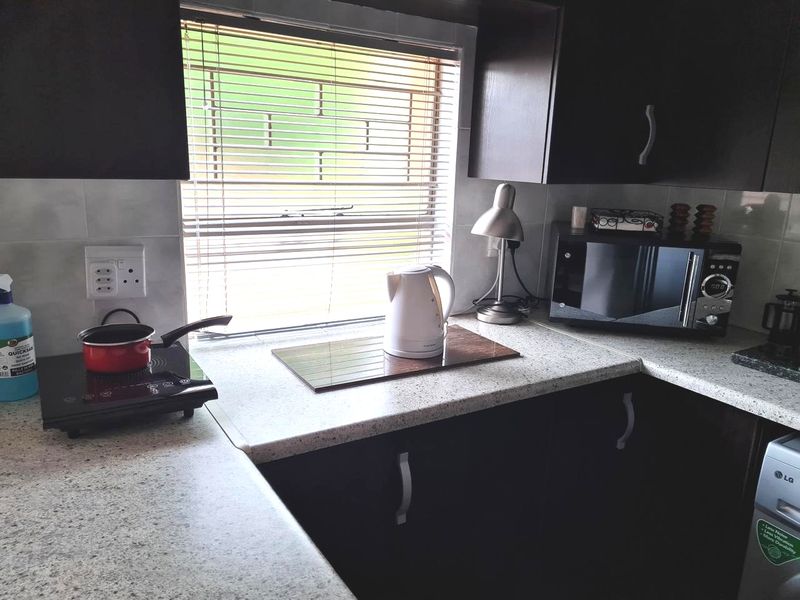A functional kitchen area featuring dark wood cabinetry, light-toned laminate countertops, and a tiled backsplash with a window providing natural light.