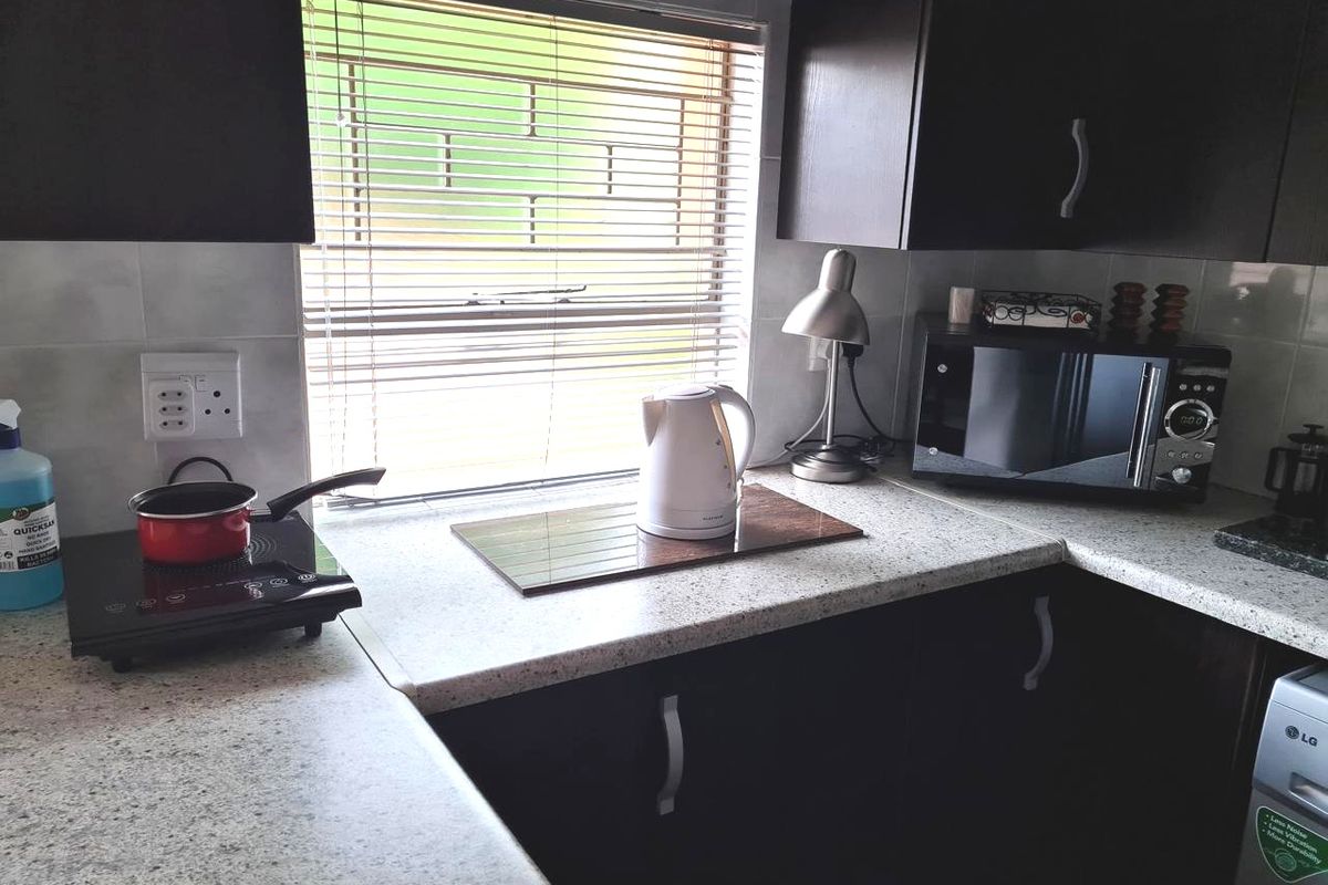 A functional kitchen area featuring dark wood cabinetry, light-toned laminate countertops, and a tiled backsplash with a window providing natural light.