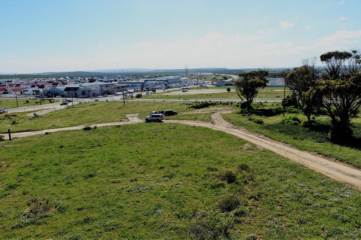 An aerial view of a vacant residential plot featuring natural vegetation, mature trees, and an existing dirt access track.