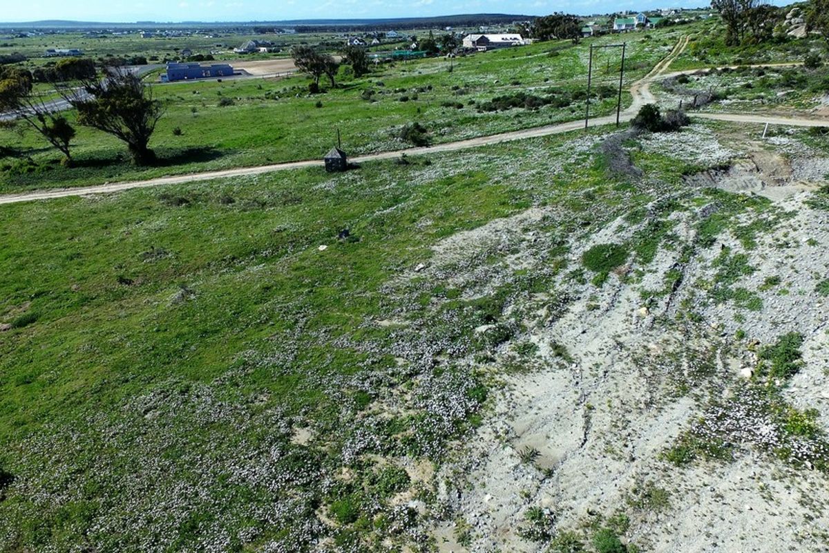 An aerial view of a large, undeveloped residential plot featuring natural vegetation, a dirt access road, and visible overhead power lines.