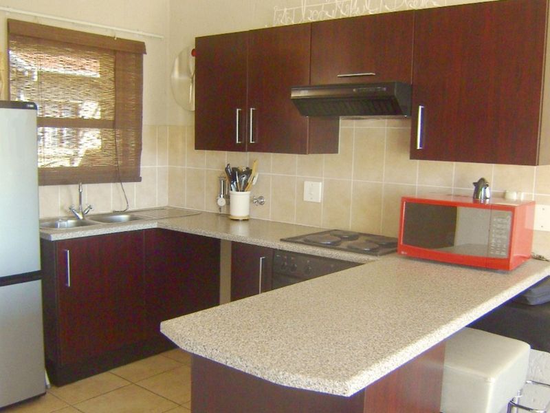 Compact kitchen featuring dark wood cabinetry, laminate countertops, tiled backsplash, and integrated cooking appliances, offering a functional layout for an apartment.