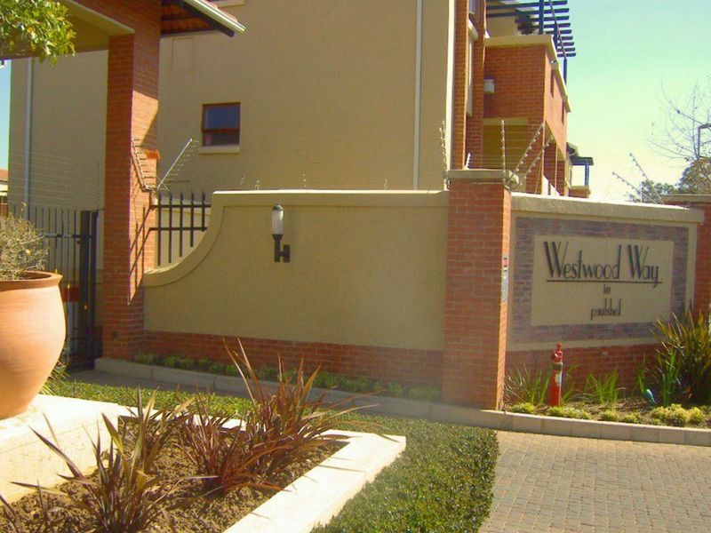 Entrance view of Westwood Way complex featuring brick boundary walls, electric fencing, and paved driveway access.