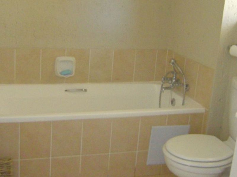 A dated bathroom featuring a built-in bathtub with tiled surround, a standard toilet, and chrome fixtures, requiring cosmetic updates to modernize the space.
