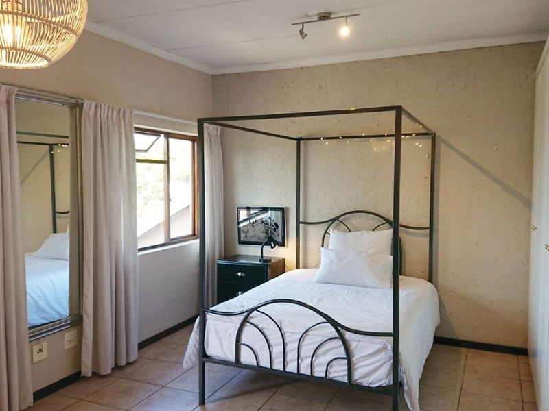 A bedroom featuring tiled flooring, built-in cupboards, and ceiling track lighting, offering a functional space with neutral wall finishes.