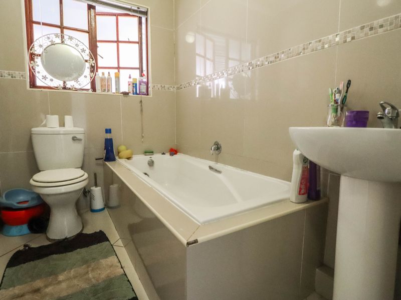 A functional bathroom featuring a pedestal basin, built-in bathtub, and tiled finishes throughout, offering a practical layout for daily use.