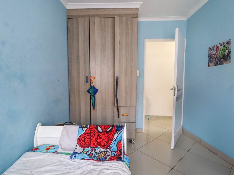 A bedroom featuring tiled flooring, a built-in wooden wardrobe, and coved ceiling details, currently finished in a light blue paint.