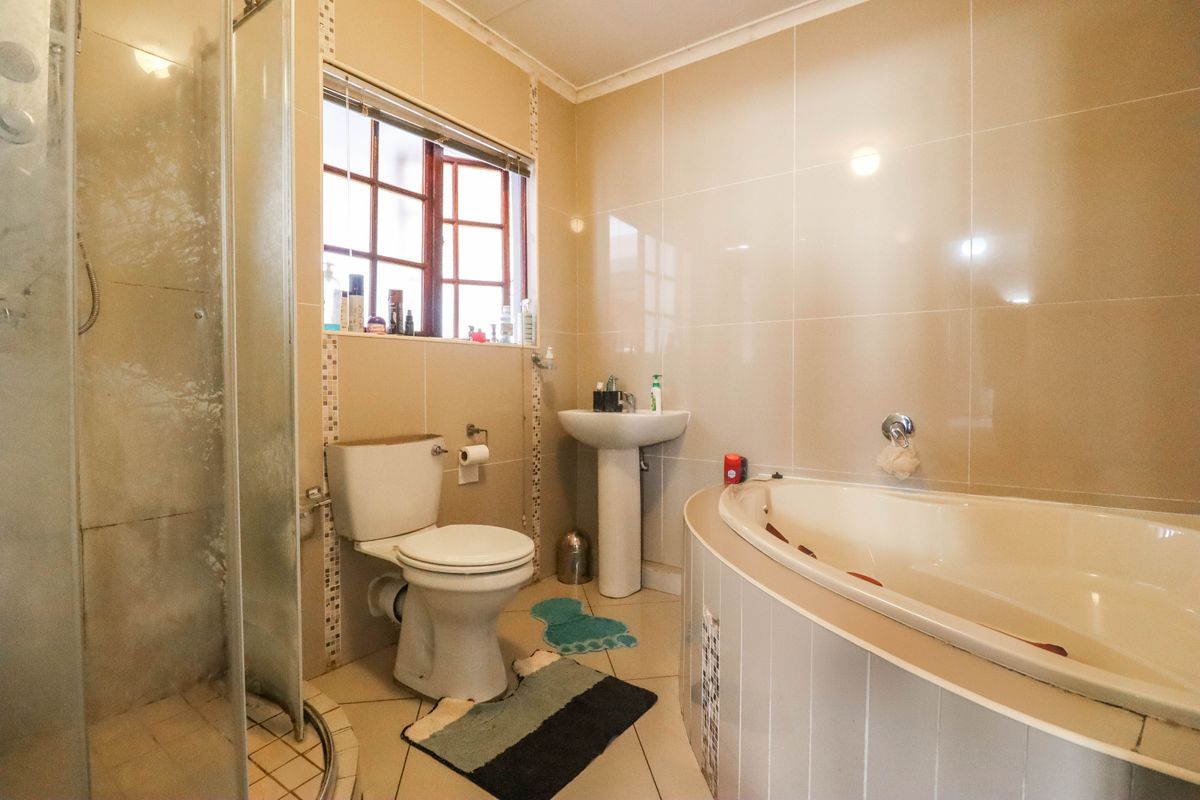 A functional bathroom featuring a corner bathtub, separate shower enclosure, pedestal basin, and neutral wall tiling.