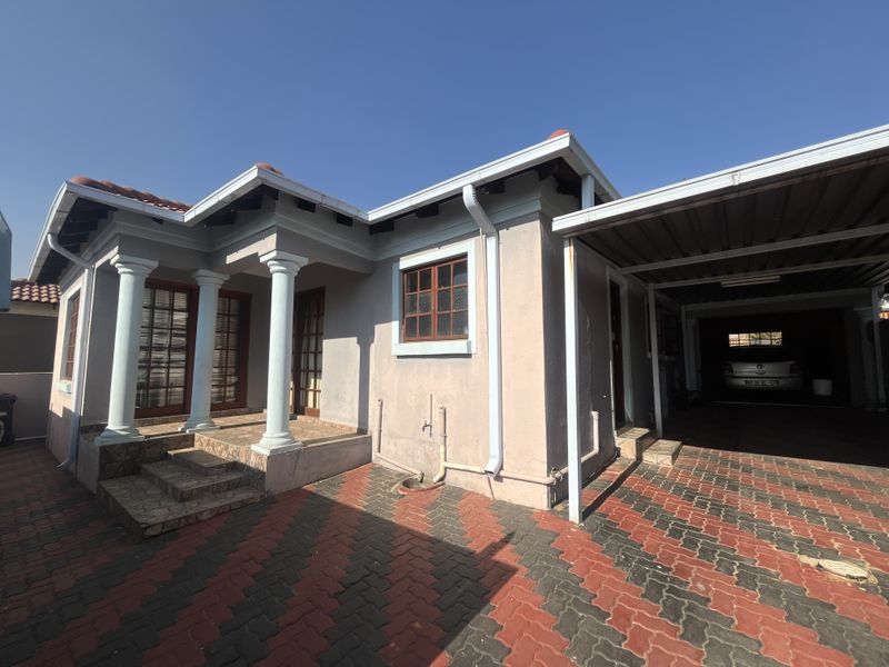 Front elevation of a house featuring a paved driveway, attached carport, and a covered entrance porch with decorative columns.