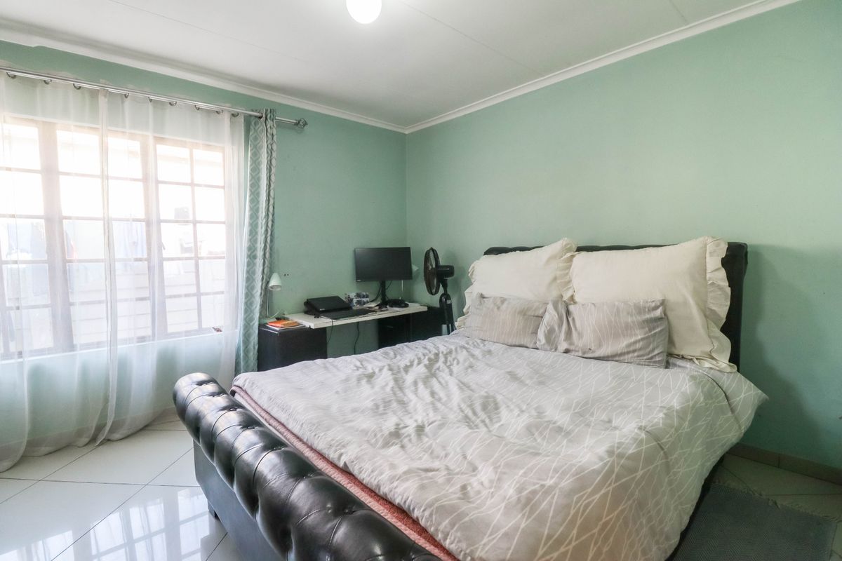 A bedroom featuring tiled flooring, light green walls, and a window allowing natural light, providing a functional space for rest.