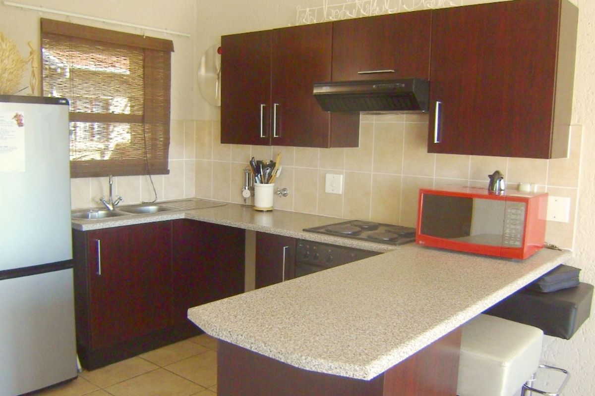 Compact kitchen featuring dark wood cabinetry, laminate countertops, tiled backsplash, and integrated cooking appliances, offering a functional layout for an apartment.