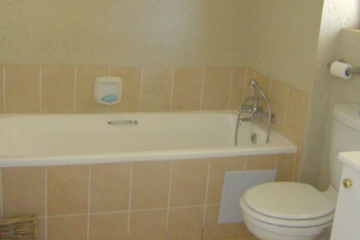 A dated bathroom featuring a built-in bathtub with tiled surround, a standard toilet, and chrome fixtures, requiring cosmetic updates to modernize the space.