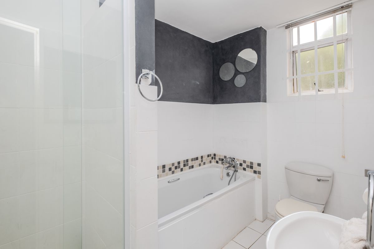 A functional bathroom featuring a separate shower enclosure, bathtub, toilet, and pedestal basin with tiled finishes and a window for natural light.